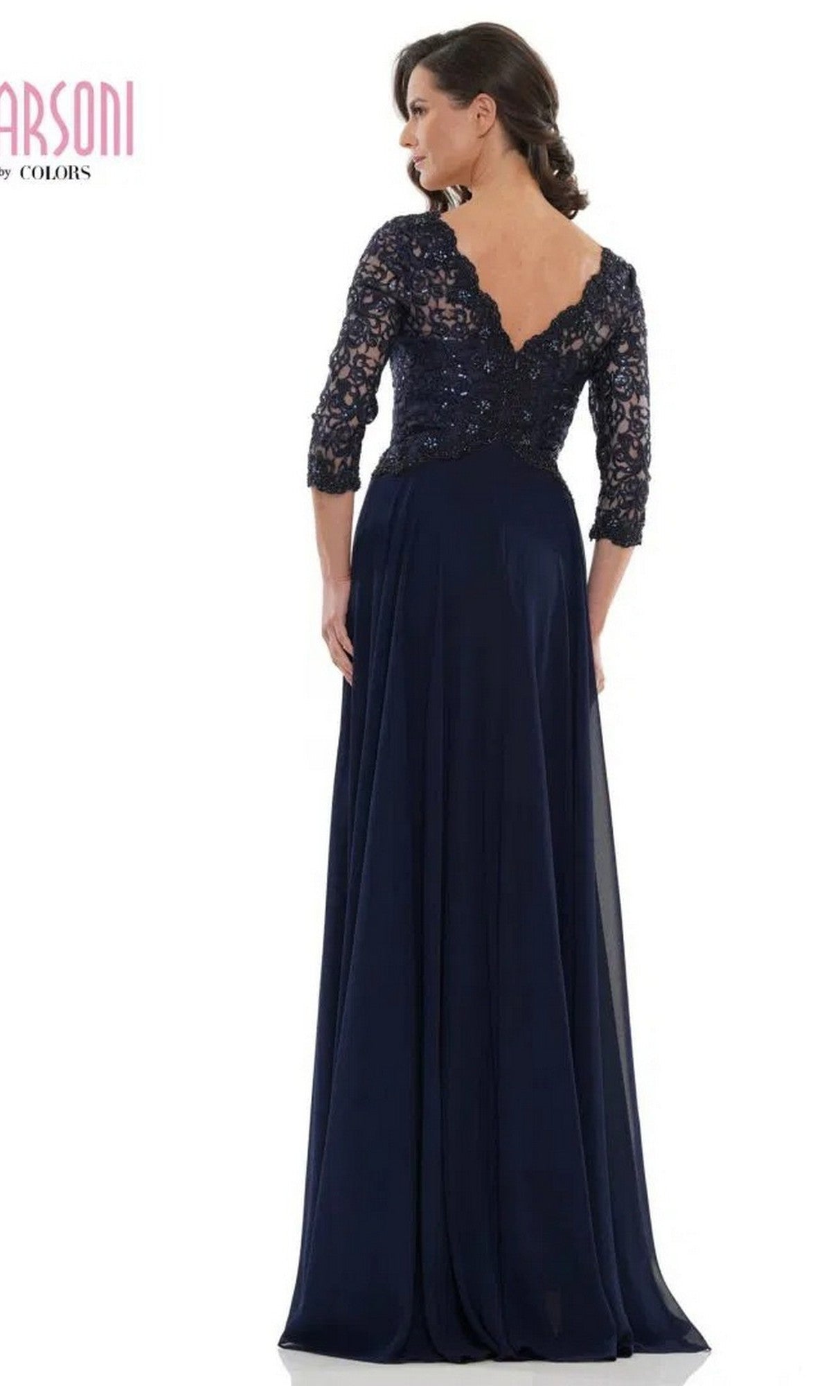A woman stands facing away, wearing the Marsoni M225 long formal dress in navy, featuring lace-embroidered bodice, lace sleeves, deep V-back, and a flowing chiffon A-line skirt.